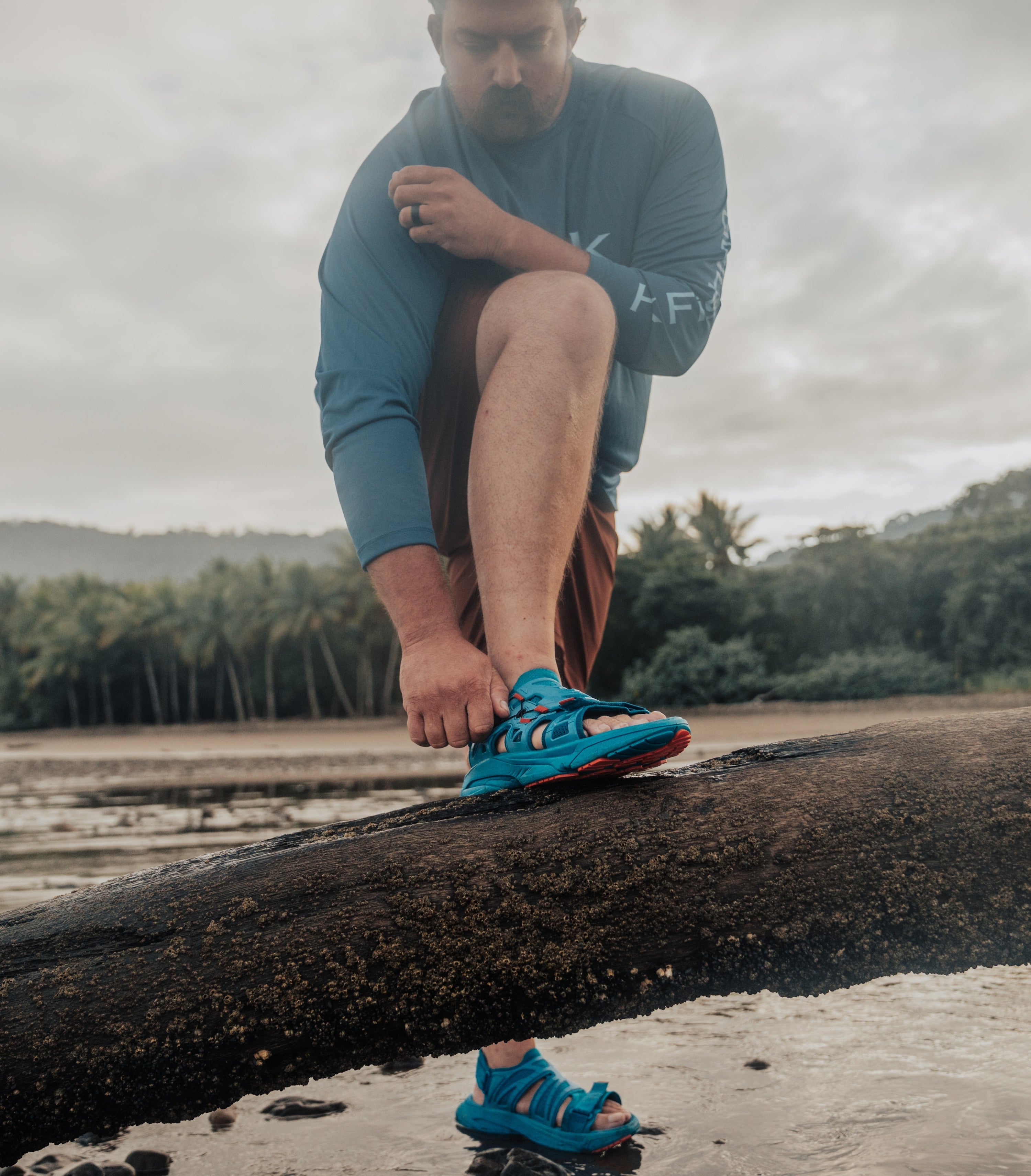 a man with his foot up on a log adjusting his amento sandals