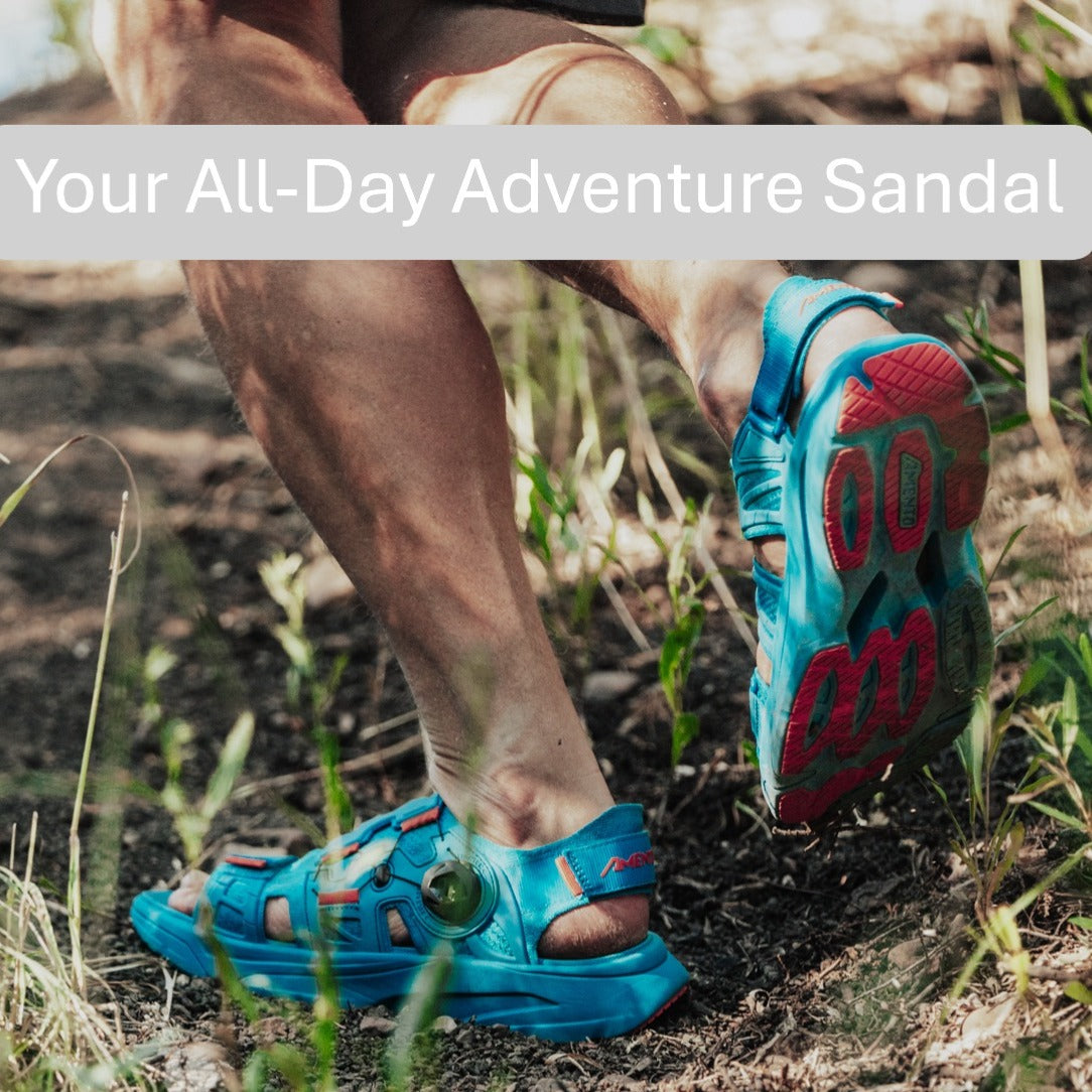 "Person hiking through forest trail wearing bright blue Amento Martlett adventure sandals with Orange traction outsole"