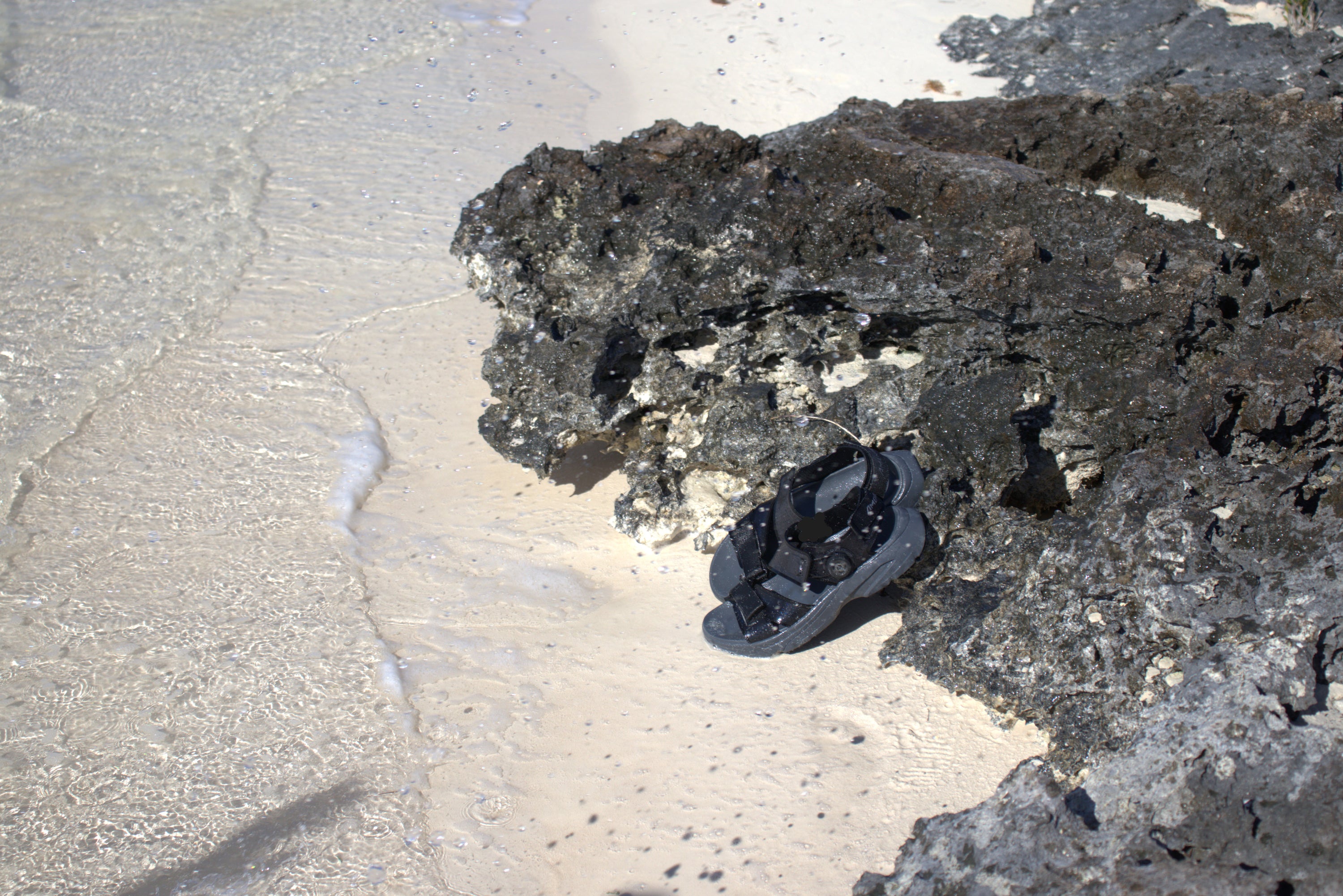 pair of men's Wingra sandals in black on rocky shoreline by sand and surf